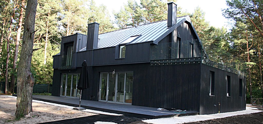 Nowoczesny czarny dom jednorodzinny z dużymi przeszkleniami, położony w otoczeniu sosnowego lasu.